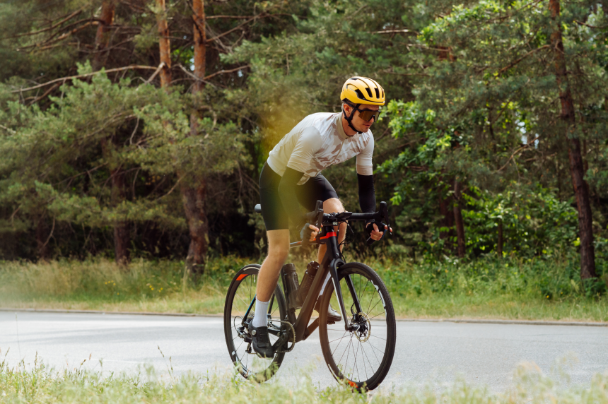Professional cyclist quickly rides in the woods on an asphalt road outside the city, side view.