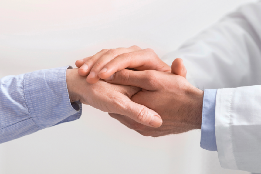 Older people healthcare support concept. Doctor holding hand of senior woman at medical visit, close up