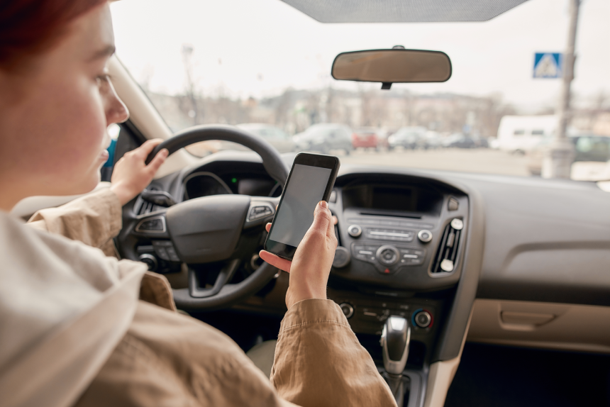 Distracted young female driver looking at the screen of her mobile phone while driving a car
