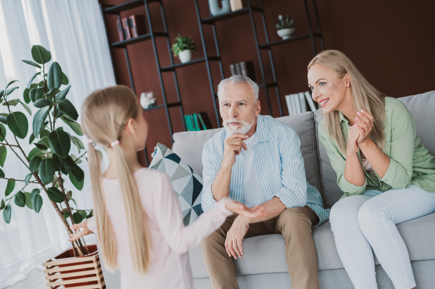 Playful family moment as a young girl chats with her parents and grandfather in a cozy living room filled with plants books and stylish shelves