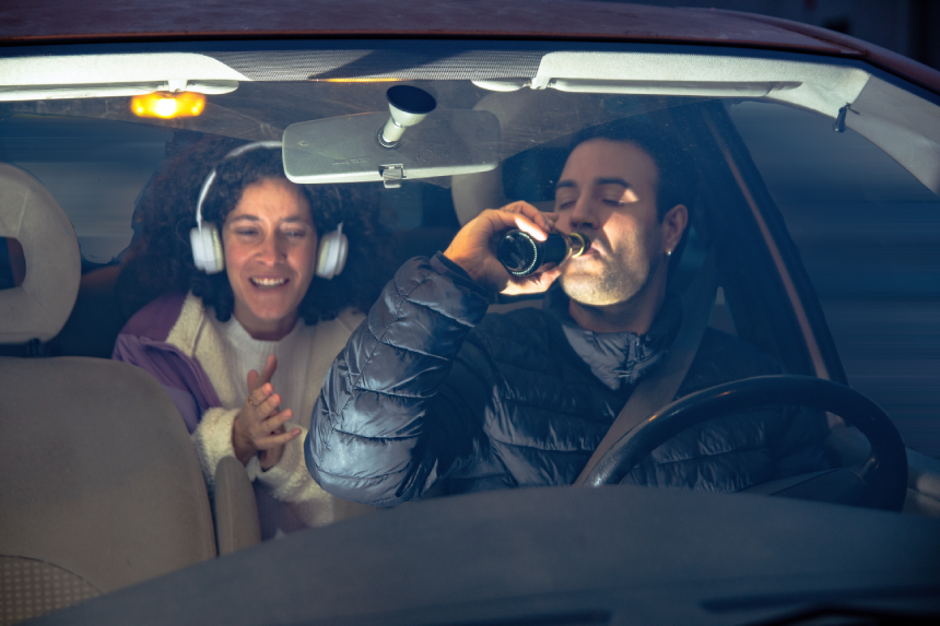 Driver drinking beer while passenger looking on happily