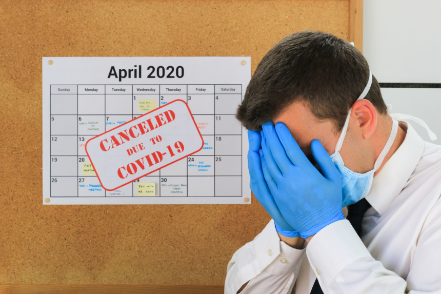 Business man, wearing a chirurgical mask and gloves, reacts to a "Canceled due to Covid-19" message placed on top of an April-2020 calendar