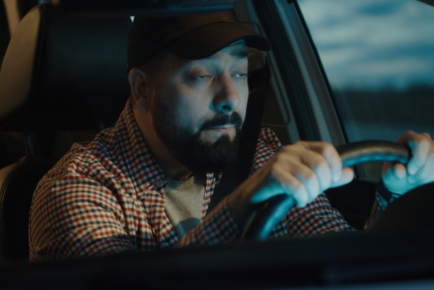 Medium shot of a sleepy man slapping himself while driving his car at night