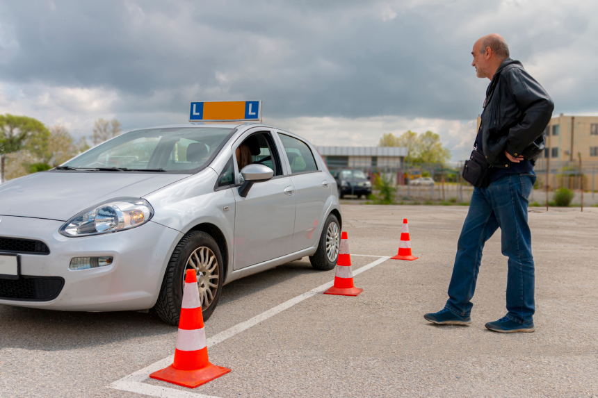 Driving instuctor watching teenage girl practising driving on the polygon with cones at the day