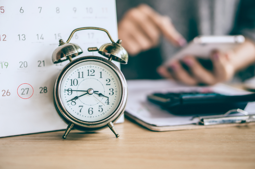 due date calendar and alarm clock with blur business woman hand calculating monthly expenses during tax season.
