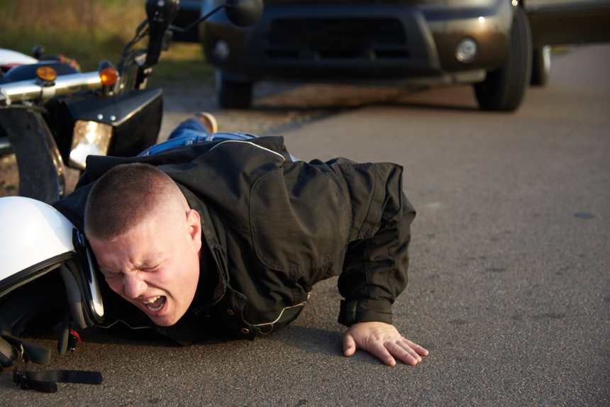 A motorcyclist lies on the asphalt near a motorcycle and car, the theme of road accidents.