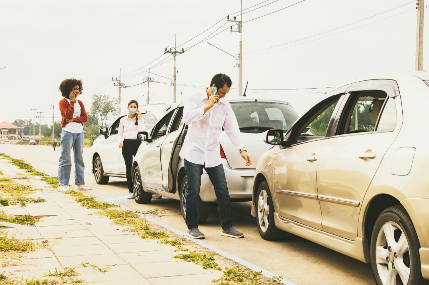 Man who was involved in a three vehicle collision standing stressed looking at the damage use phone to call the insurance company to clear and assess the initial damage to the other two women's cars