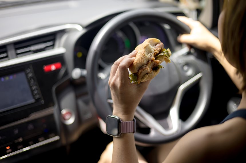 Woman is eating a hamburger while driving to work in the morning