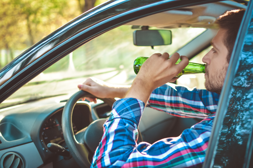 Drunk young man driving a car with a bottle of beer. Don't drink and drive concept.