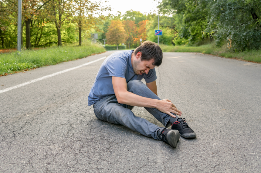 Injured man has broken leg and is sitting on road.