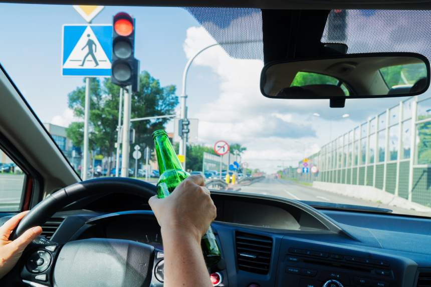 Someone hands driving and holding a bottle with alchohol. Drunk driving concept