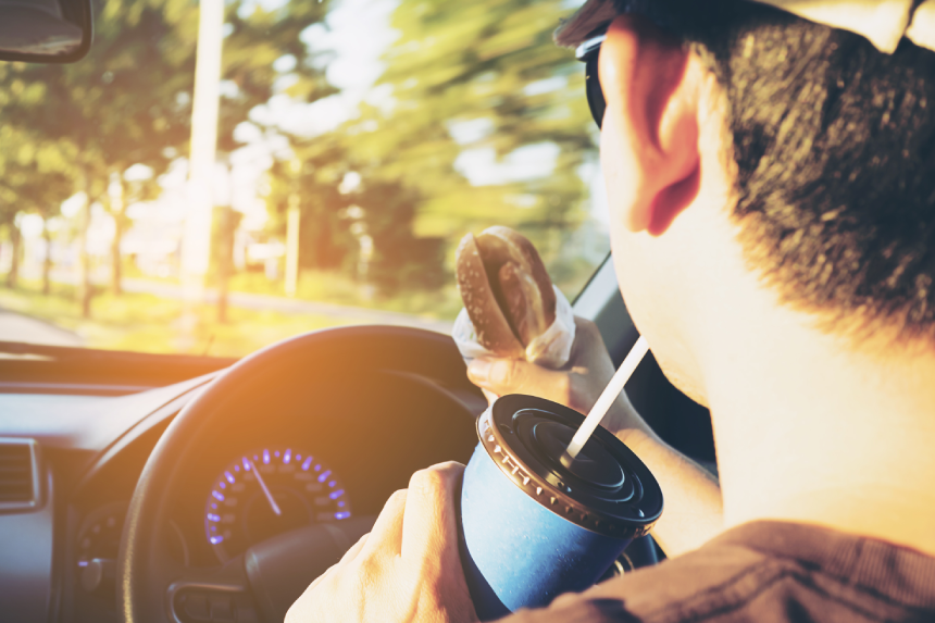 Man is dangerously eating hot dog and cold drink while driving a car