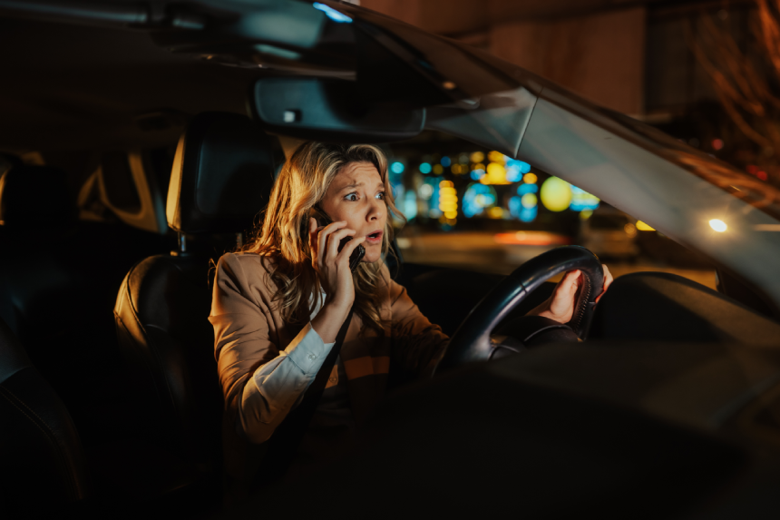 Woman feeling shocked, fearful, and panicking during a phone call while driving a car at night, representing distracted driving