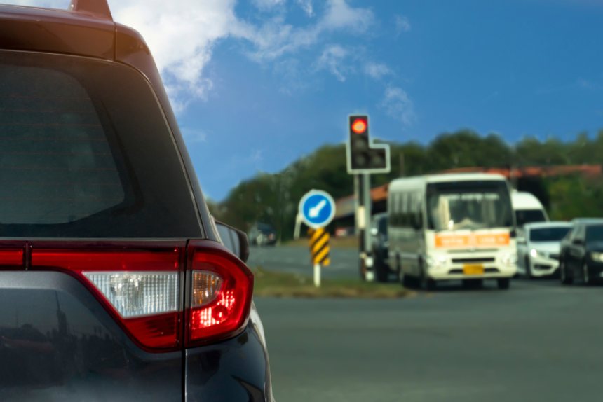Rear side of car driving on the asphalt road. Stop and open turn on light brake by traffic light signal. Blurred of other cars in the upcountry with trees.