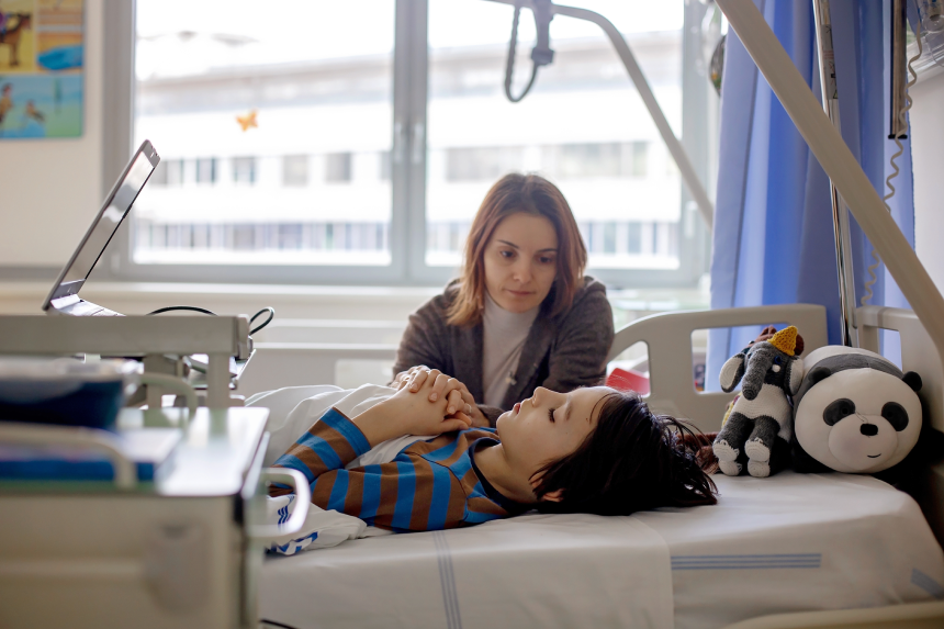 Preteen child, boy, lying in hospital with fractured thoracic spine, vertebralis, mother sitting next to his bed