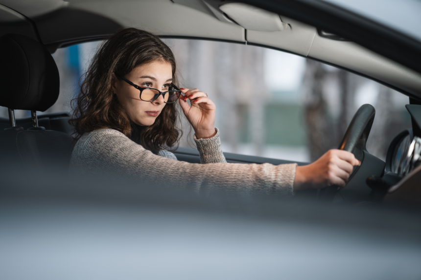 woman have problems with driving due to blurry vision, hand holding eyeglasses. A young beautiful girl driver rides in a car, carefully looking at the road