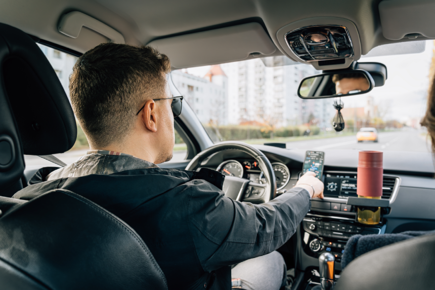 A man uses a phone installed in the holder while driving