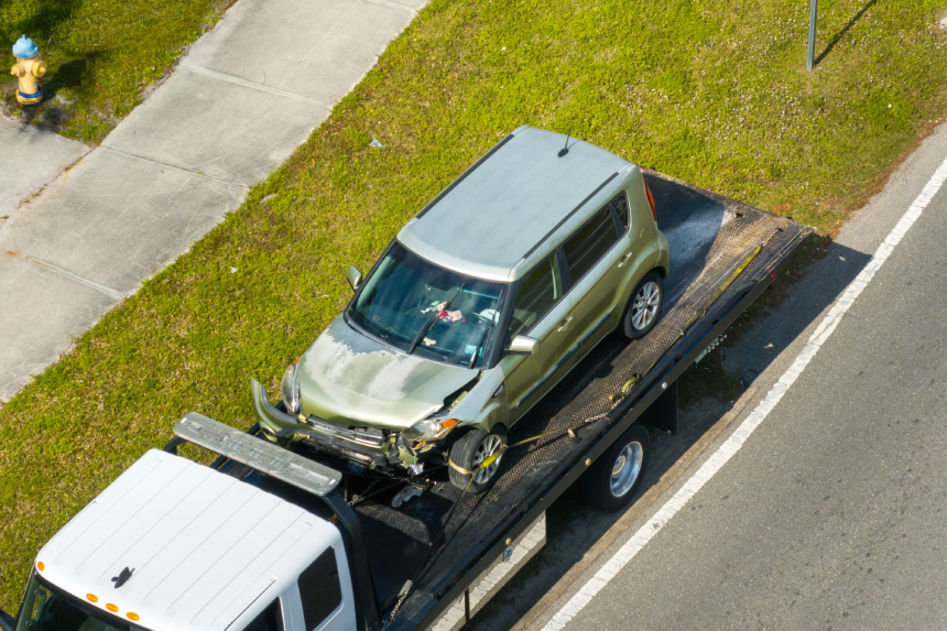 Tow truck hauling smashed vehicle on car accident site. Emergency services responding to traffic crash on American street.