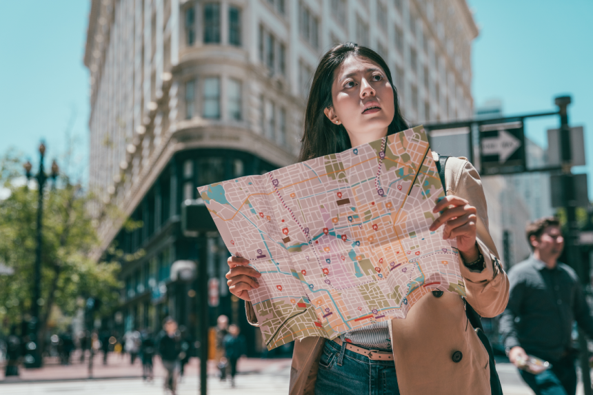 pretty young female holding a guide map and looking lost in the middle of streets in a big city.