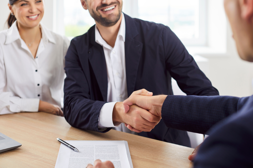 Real estate agent or realtor is shaking hands with a couple, sealing the deal for new home, house or property.