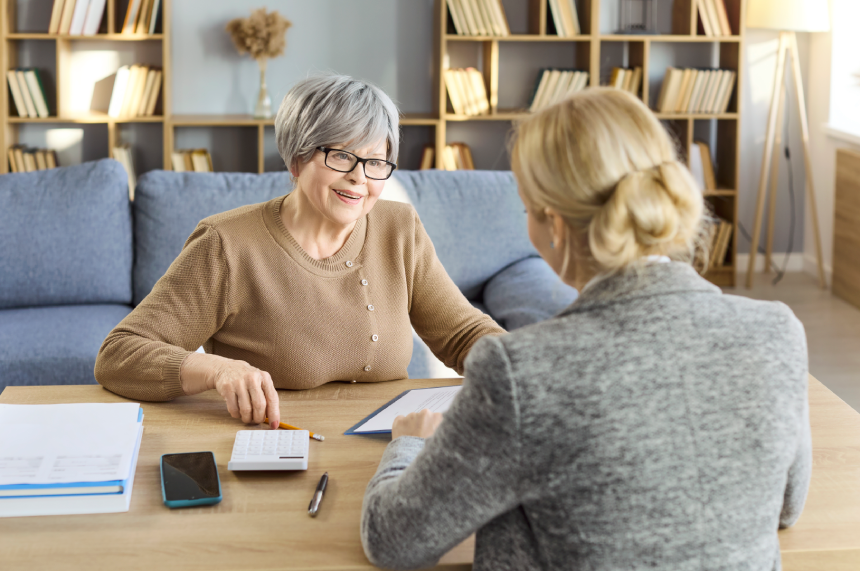 Senior woman and advisor in consultation. At home client reviews paperwork with an advisor, discussing savings insurance and estate planning with a calculator.