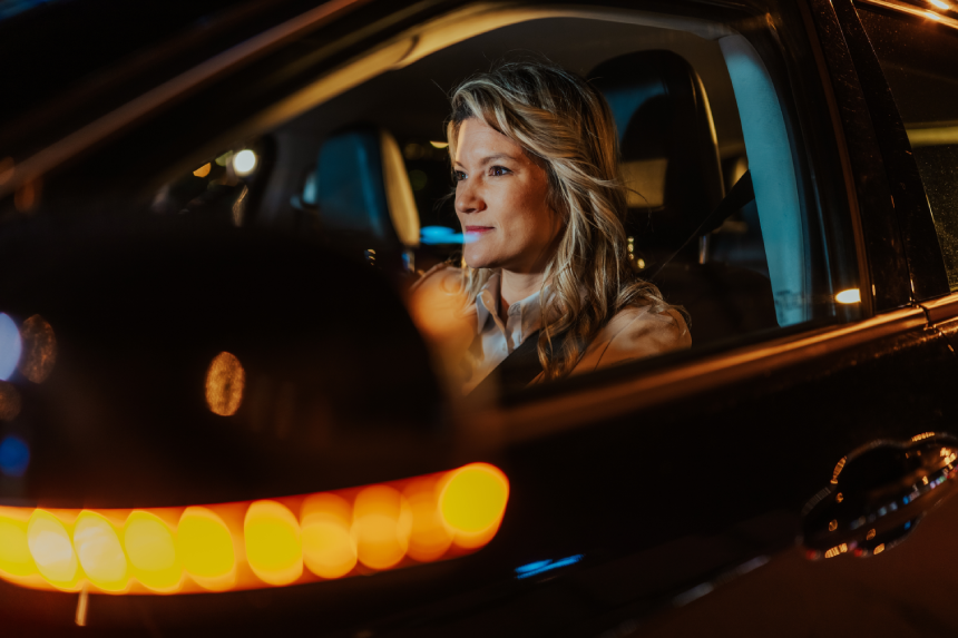 Woman driving car at night, traveling through city streets. She is focused on the road, commuting home or to work
