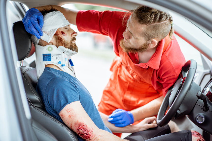 Medics wearing neck corset to an injured man sitting in the car after the road accident, providing emergency medical assistance