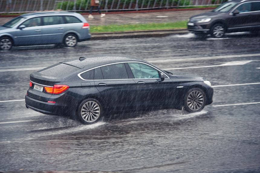 Car driving fast on wet road, driving through puddle during heavy rain.