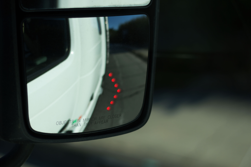 The rearview mirror shows red warning lights indicating the presence of vehicles in the driver\'s blind spot. This safety feature enhances visibility during lane changes.