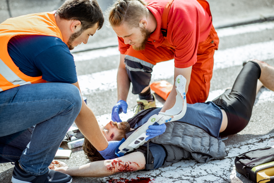Ambluence workers applying emergency care to the injured bleeding man lying on the pedestrian crossing after the road accident