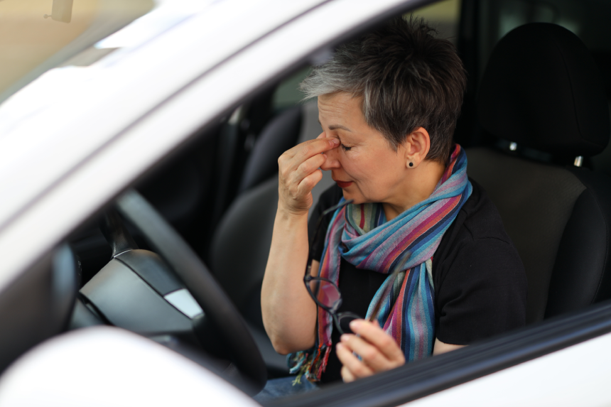 A woman in a parked car takes off her glasses and rubs her eyes. Driving fatigue and rest.