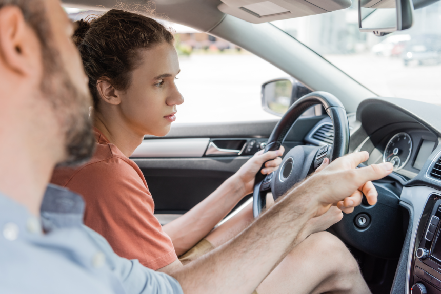 bearded father pointing at speedometer while teaching teenage son how to drive car