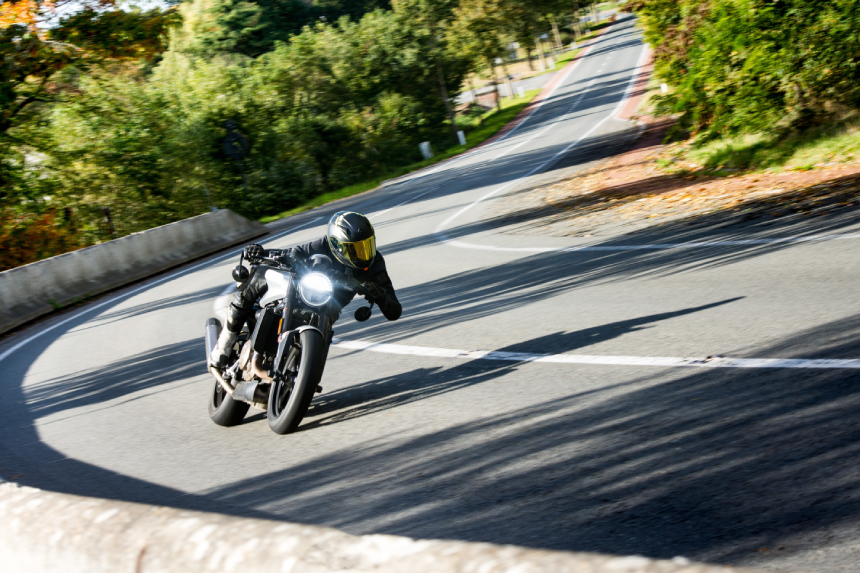 A skilled motorcyclist leans into a sharp turn on a scenic, tree-lined road, showcasing speed and control.
