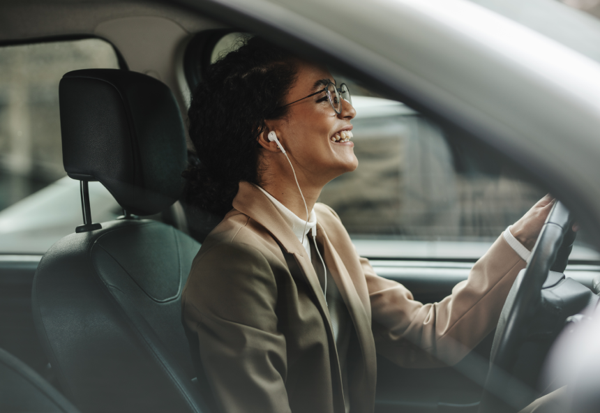 Businesswoman with earphones driving her car to office and smiling. Woman enjoying listening to music while driving to work.