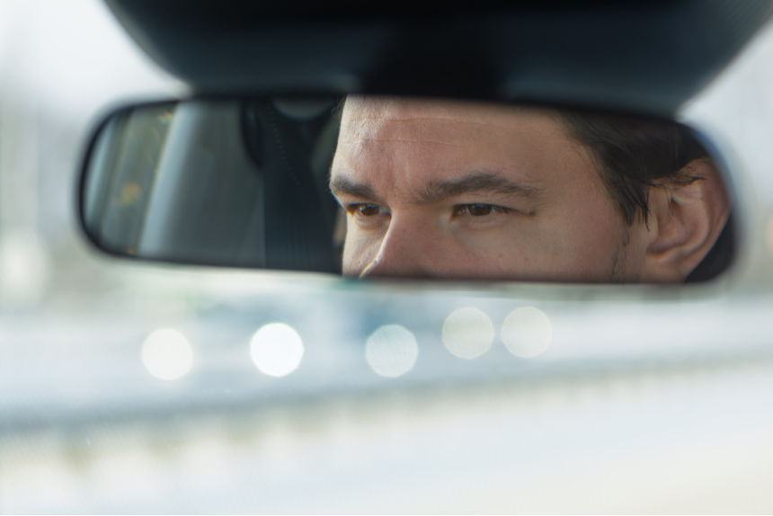Focused driver eyes in rearview mirror convey concentration on road safety and situational awareness during morning commute.