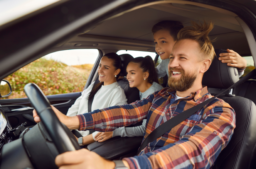 Portrait of happy laughing smiling family of four with children riding in modern car traveling by automobile together enjoying vacation or road trip on weekend.