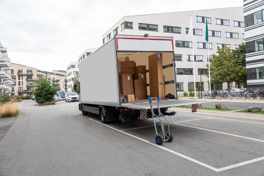 White empty delivery truck with tailgate open with goods in the cargo hold in front of an office building