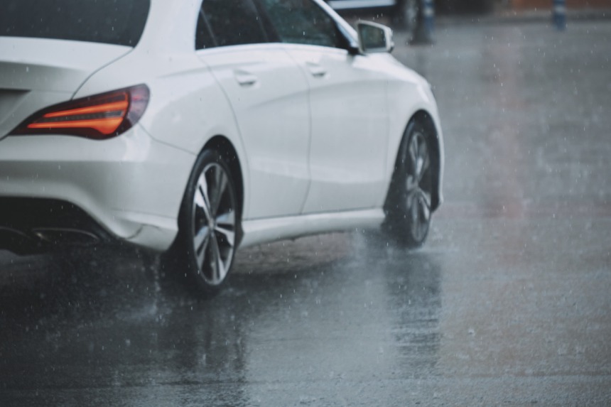 White car driving on rainy road with water splash during a storm.