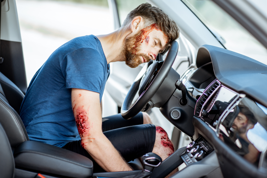 Injured man with a broken head and bleeding wounds sitting on the driver seat without consciousness after the road accident inside the car