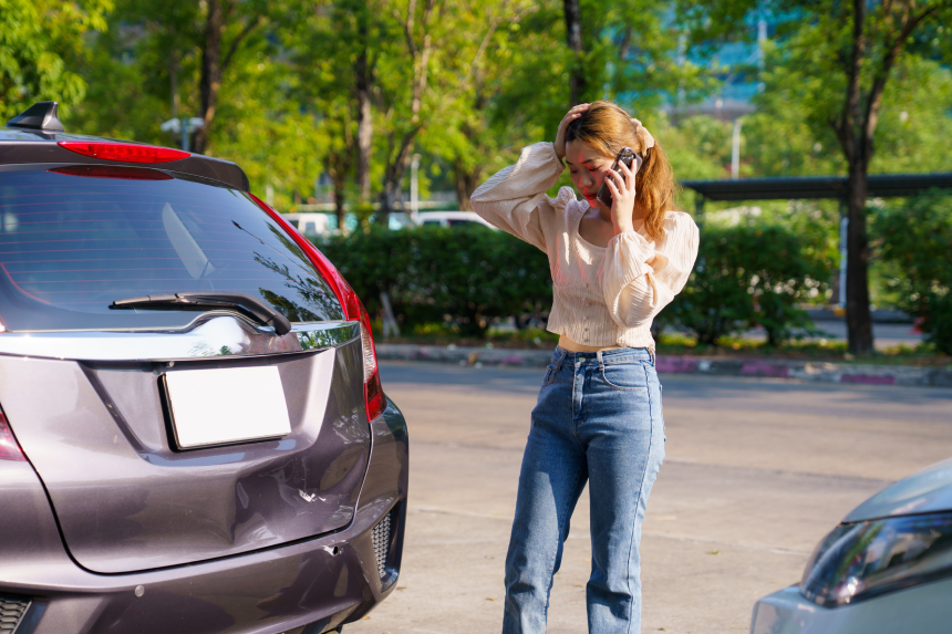 Distressed Asian female calling her car insurance company after a minor crash.
