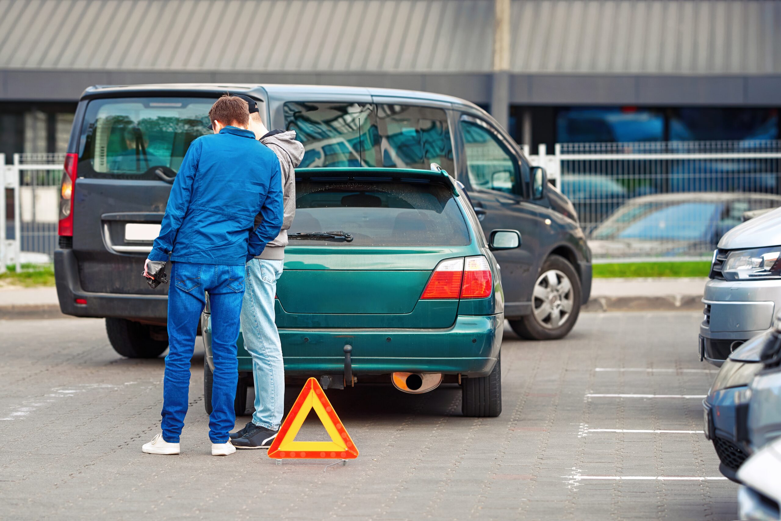 Car accident in parking lot, men set up red warning triangle after collision in parking area. Parking accident due reckless and distracted driving on tight parking lot.