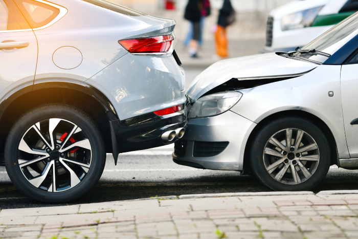 Rear end collision between two cars on urban street with visible damage to bumper and hood, traffic accident.